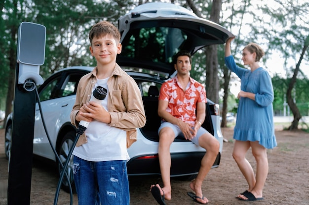 Menino segurando um carregador EV e apontando para a câmera com sua família Perpetual