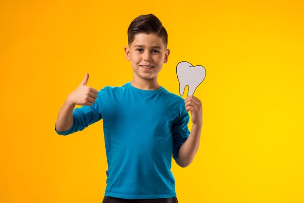 Foto menino segurando um dente de papel e mostrando o polegar para cima gesto conceito de saúde dental