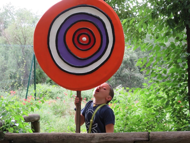 Foto menino segurando um pirulito de brinquedo enquanto está de pé contra as árvores no parque