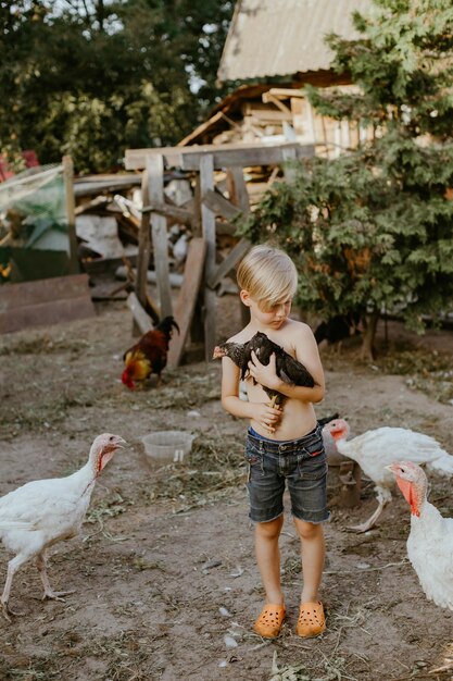 Menino sem camisa segurando uma galinha na fazenda