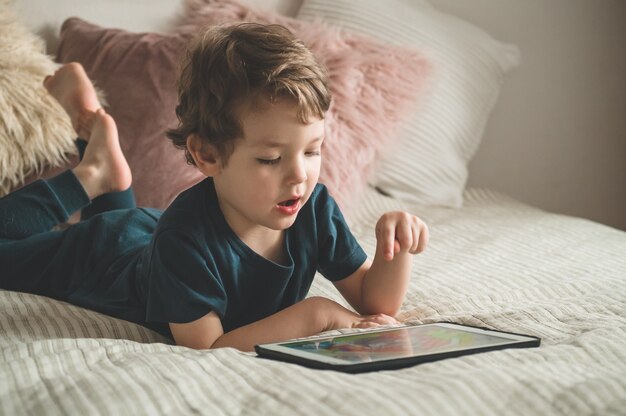 Menino sentado com um tablet na cama