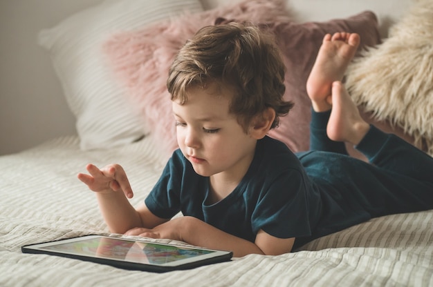 Menino sentado com um tablet na cama