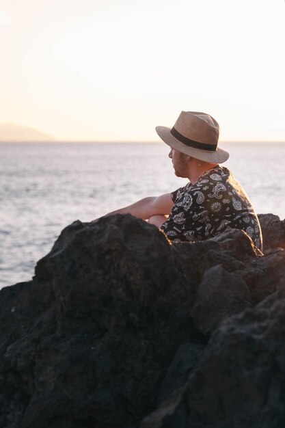 Menino sentado em frente ao mar aprecia o pôr do sol