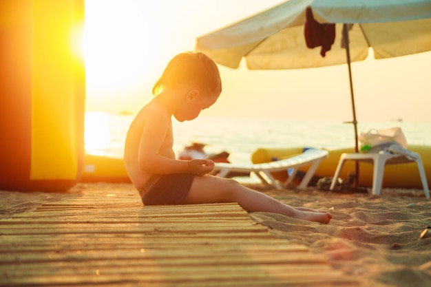 Menino sentado na praia ao pôr do sol