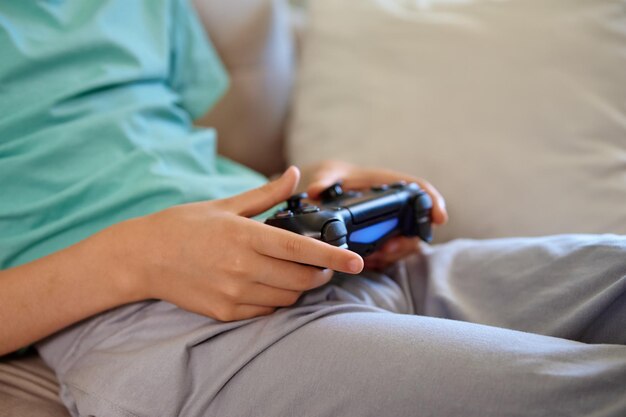 Menino sentado no sofá na sala de estar e jogando videogame no console com joyctick gamepad em seu ha