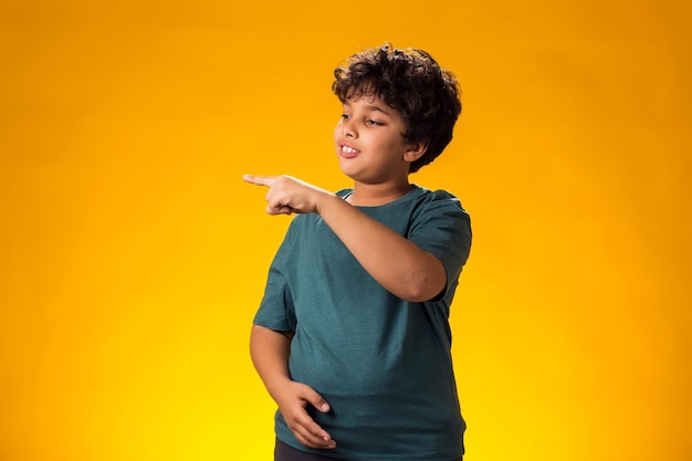 Foto menino sorridente apontando para um lugar vazio em fundo amarelo conceito de publicidade