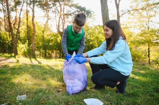 Menino sorridente catando lixo no parque com sua mãe. Conceito de voluntário.