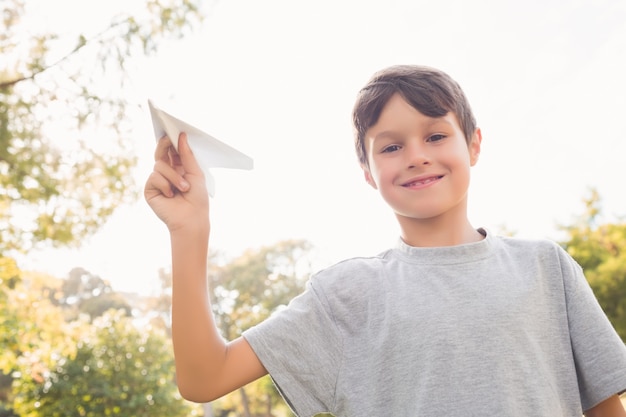 Menino sorridente com avião de papel no parque