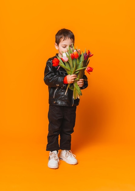 Menino sorridente com buquê de flores de primavera de tulipas isoladas em amarelo garotinho segurando tulipas