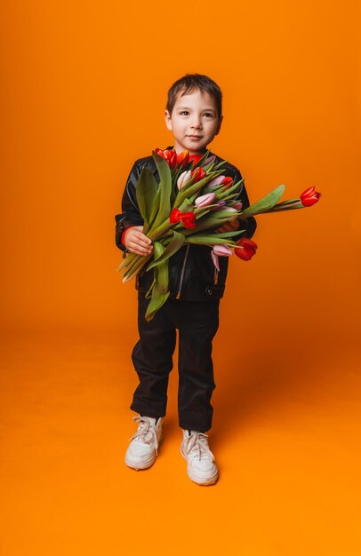 Menino sorridente com buquê de flores de primavera de tulipas isoladas em amarelo garotinho segurando tulipas