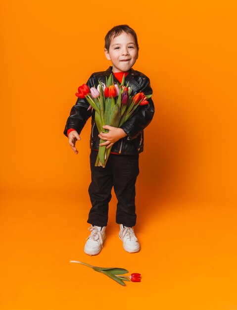 Menino sorridente com buquê de flores de primavera de tulipas isoladas em amarelo garotinho segurando tulipas