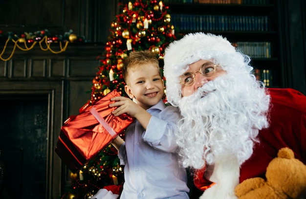 Menino sorridente com Papai Noel contra a árvore de Natal em casa