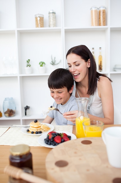 Menino sorridente comendo panquecas com sua mãe para o café da manhã