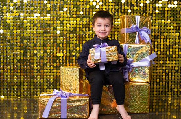 Menino sorridente criança segurando a caixa de presente no fundo com lantejoulas brilhantes de ouro, paillettes.