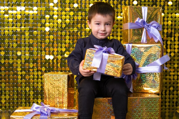Menino sorridente criança segurando uma caixa de presente no fundo com paillettes de lantejoulas brilhantes douradas