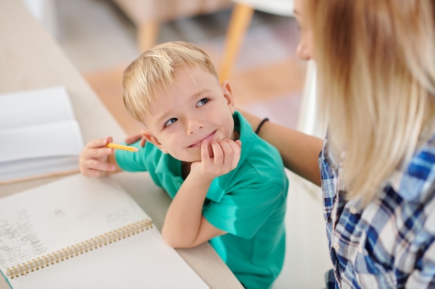 Menino sorridente e feliz olhando para a mãe explicando um tópico difícil de matemática