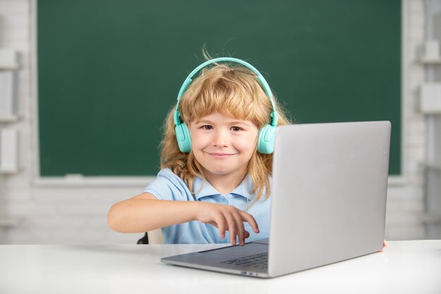 Menino sorridente em fones de ouvido usando um laptop e estudar on-line com o professor de videochamada na escola