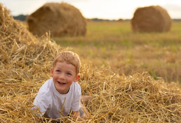 menino sorridente feliz na pilha de palha agosto verão