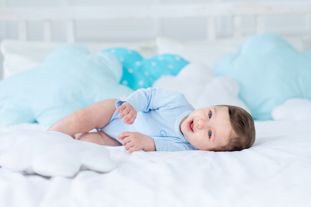 Menino sorridente ou rindo na cama para dormir, bebê feliz e saudável em macacão azul