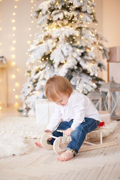 Menino sorridente parado perto da árvore de natal feliz ano novo e feliz natal