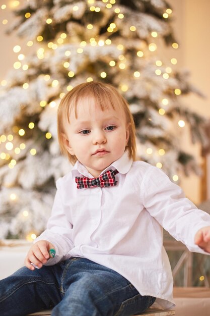 Menino sorridente parado perto da árvore de natal feliz ano novo e feliz natal