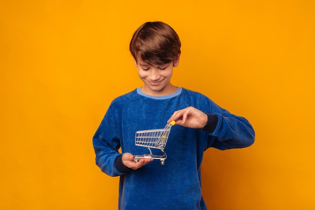 Menino sorridente quer aprender sobre finanças enquanto segura um carrinho de compras