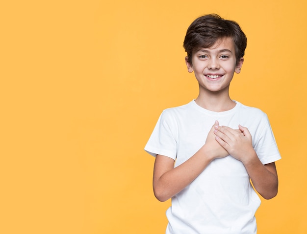 Menino sorridente, segurando as mãos no lugar do coração