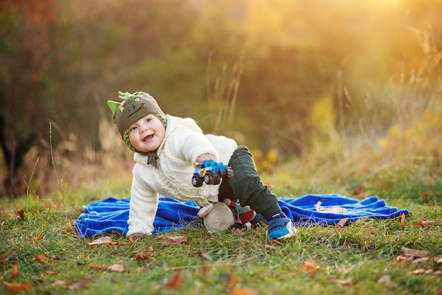 Menino sorridente, sentado em uma manta azul e brincando com brinquedos em um gramado verde ao pôr do sol