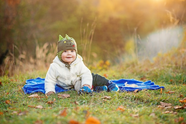 Menino sorridente, sentado em uma manta azul e brincando com brinquedos em um gramado verde ao pôr do sol