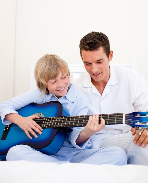 Menino sorridente tocando violão com seu pai