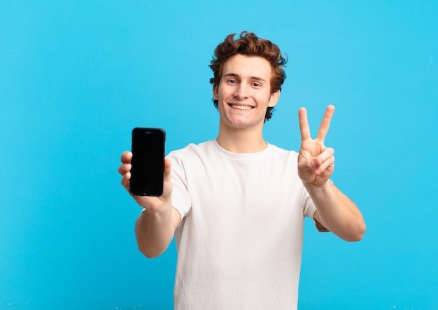 Menino sorrindo e parecendo feliz, despreocupado e positivo, gesticulando vitória ou paz com uma mão