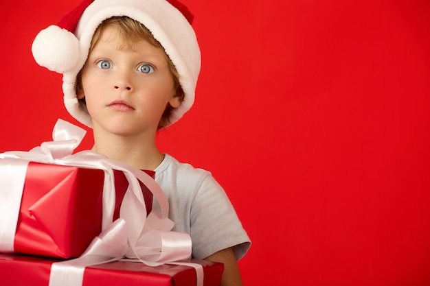 Menino surpreso com um chapéu de Papai Noel segura um presente de Natal