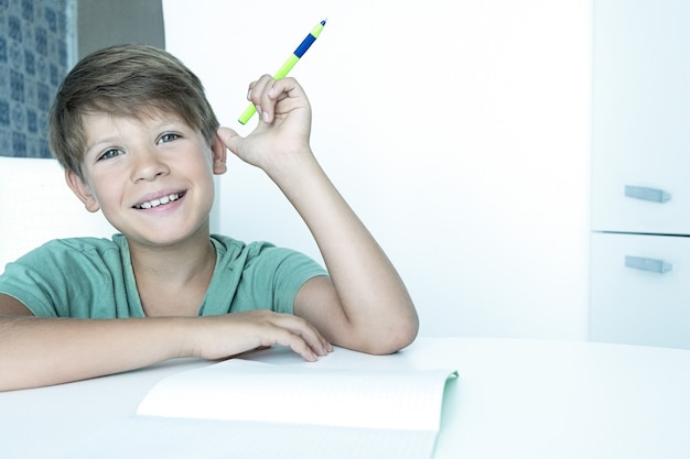 Menino triste com livro faz lição de casa da escola. De volta à escola. Estudante infeliz com livros didáticos. Ensino à distância.