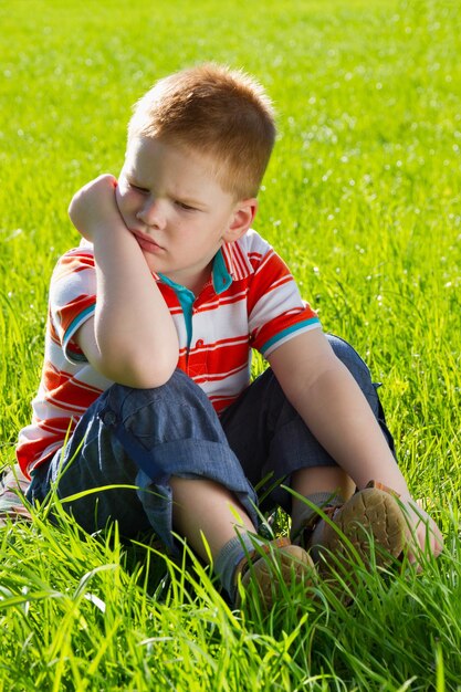 Menino triste com raiva sentado na grama