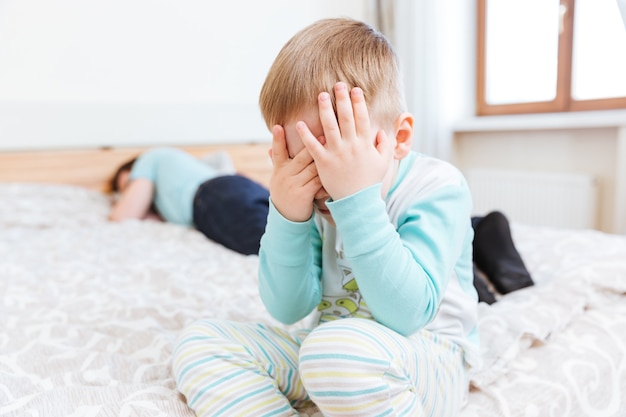 Menino triste sentado e chorando na cama enquanto seu pai está dormindo