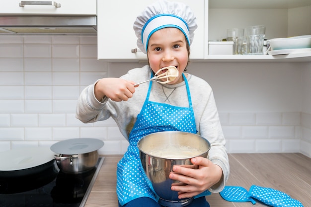 Menino usando chapéu de chef e avental assando em uma cozinha