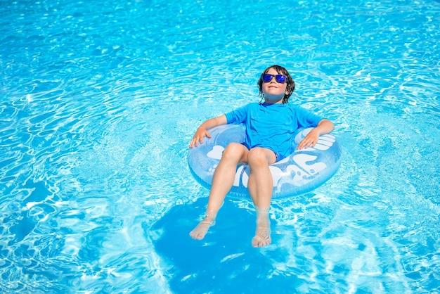 Menino usando óculos de sol relaxando em um anel de natação inflável em um dia ensolarado, passando o tempo em uma piscina aquapark resort hotel conceito de férias de verão