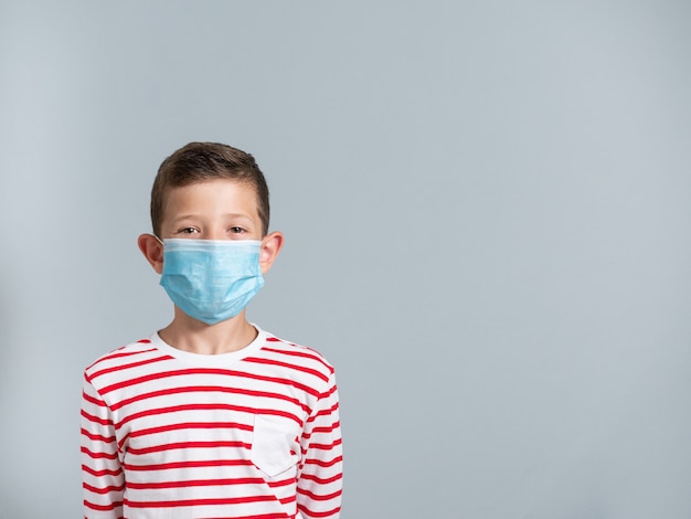 Foto menino usando uma máscara facial, conceito de proteção contra coronavírus, isolado na parede cinza