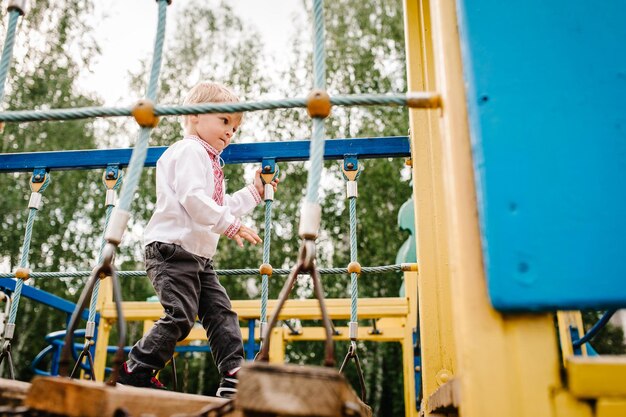 Menino vai ao playground para crianças ao ar livre em uma camisa bordada andando pelas escadas fechar dar passos perna pé comprimento total olhando para baixo