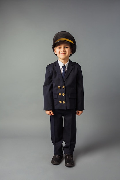Menino vestido com um uniforme de piloto preto fica no fundo cinza