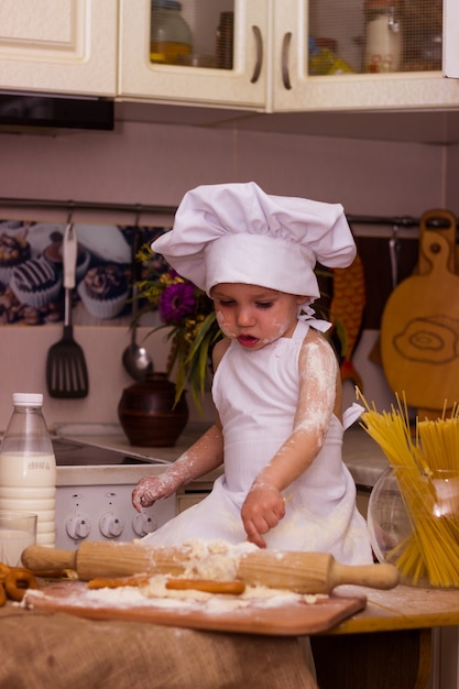 Menino vestido de cozinheiro amassando massa de farinha