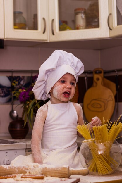 Menino vestido de cozinheiro amassando massa de farinha