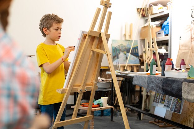 Menino vestindo camiseta amarela pintando no cavalete de desenho