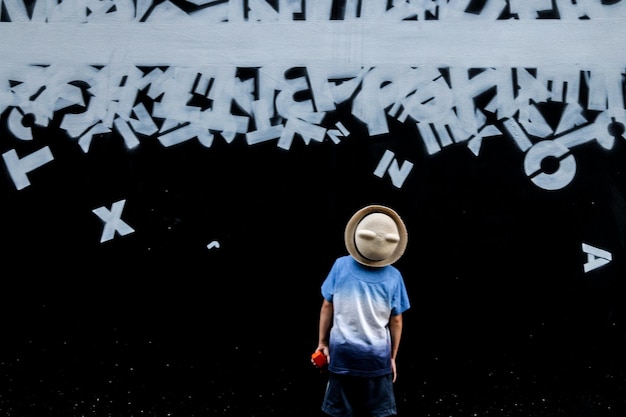 Foto menino vestindo chapéu enquanto está de pé contra graffiti