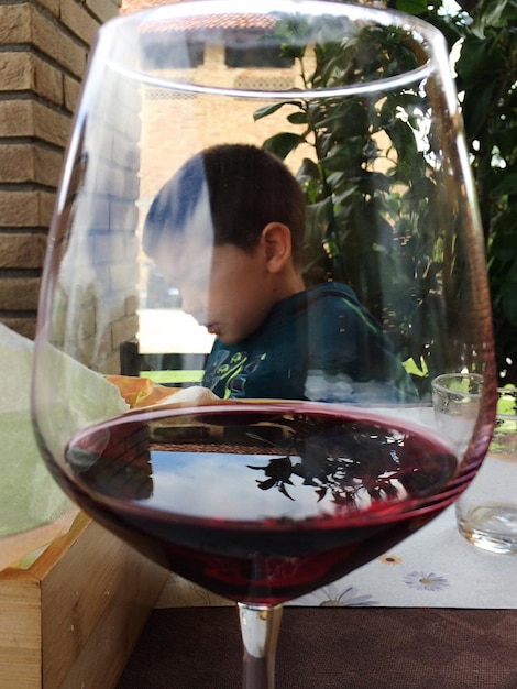 Foto menino visto através de um copo de vinho vermelho