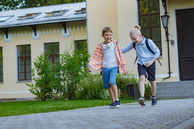 Meninos andando da escola com mochilas em dia ensolarado na porta da escola Início do ano letivo