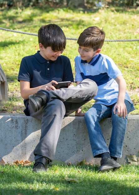 Meninos bonitos sentados no parque e jogar jogos online no telefone.