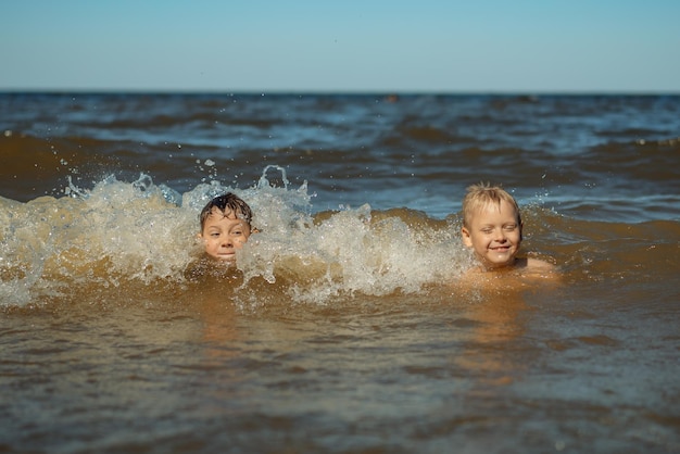 Meninos caucasianos bonitos de 78 anos nadando no mar com grandes salpicos nas ondas