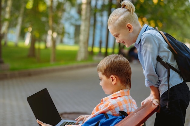 meninos caucasianos bonitos sentados no banco no parque com computador portátil Fazendo lição de casa ao ar livre depois de sch