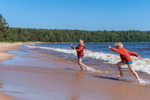 meninos caucasianos fofos vestindo moletons vermelhos e cuecas azuis correndo das ondas no lago Ladoga